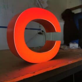 Czerwona, trójwymiarowa, świecąca litera 'e' na biurku, wykonana w Warszawie jako element reklamy świetlnej