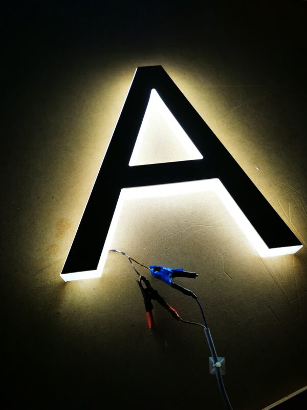 "Litera 'A' podczas testu świecenia, wykonana z 30mm bloku pleksi z frontem z pleksi złotej, ukazująca jakość i intensywność podświetlenia LED